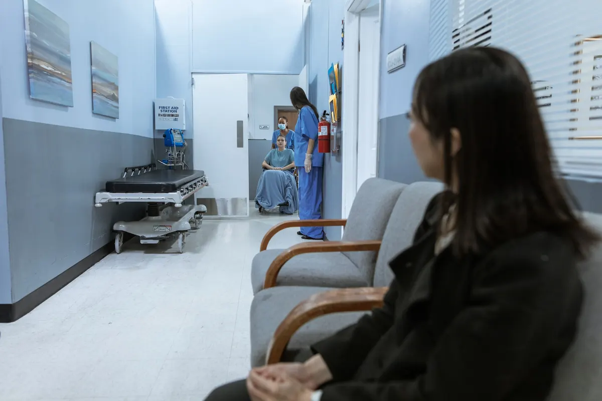 Healthcare facility waiting area with patient in blue hospital gown speaking with healthcare worker in blue scrubs