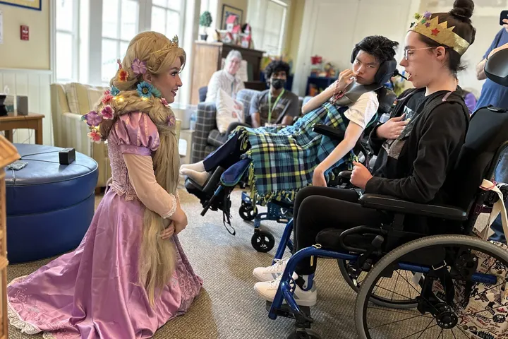 A Harmony & Healing artist dressed as Rapunzel kneels to sing with young patients in wheelchairs